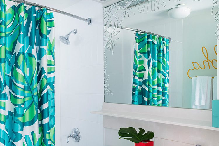 A hotel bathroom featuring a vibrant blue and green shower curtain. Our shower curtains for hotels can be made with our exclusive Impact Technology®.