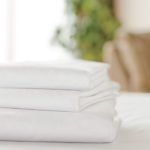 A stack of folded white Centium Satin sheets rest on a bed.