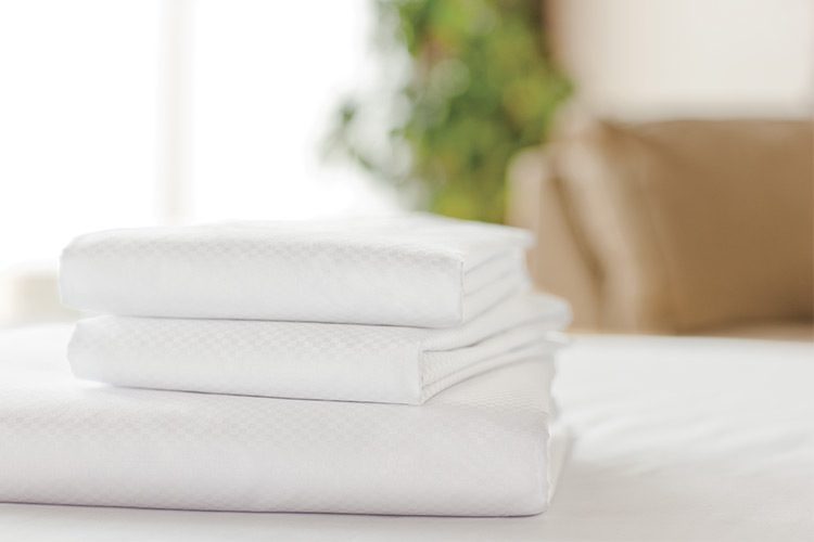 A stack of folded white Centium Satin sheets rest on a bed.
