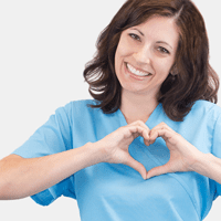Happy woman in blue hospital scrubs is making a heart symbol with her hands. The tunic shown here is part of Standard Textiles medical scrubs program. Unisex scrubs tops & pants are available in many fabrics.