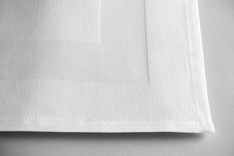 A detail shot of the corner of a Satin Band white cloth napkin.