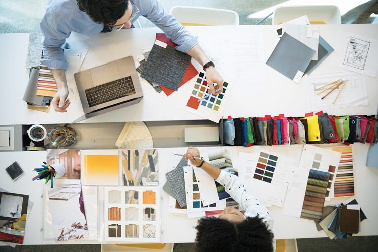 An overhead shot of two designers working, surrounded by swatches, color samples, and various fabrics.