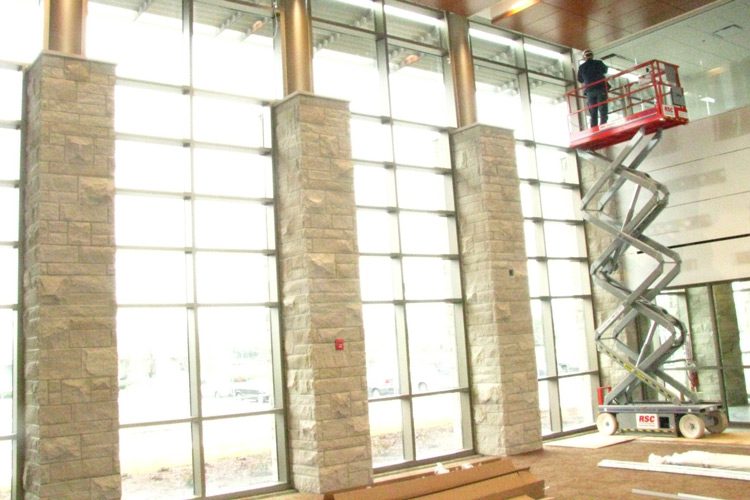 A large lobby interior showing contractors using a scissor lift to workin on installing window treatments.