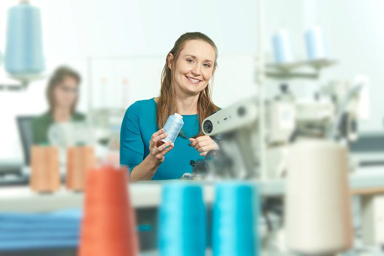 A team member sitting at a sewing machine winding a spool of blue thread.