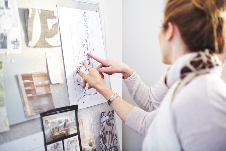 Two design consultants stand in front of a cork pin-board, featuring images and fabric inspiration for a project.