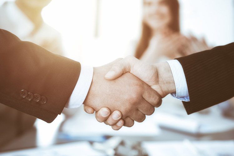Two people wearing suits shaking hands as if finalizing a business deal.