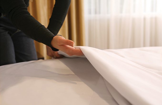 Housekeeper at a hotel making a bed with top cover and triple sheeting