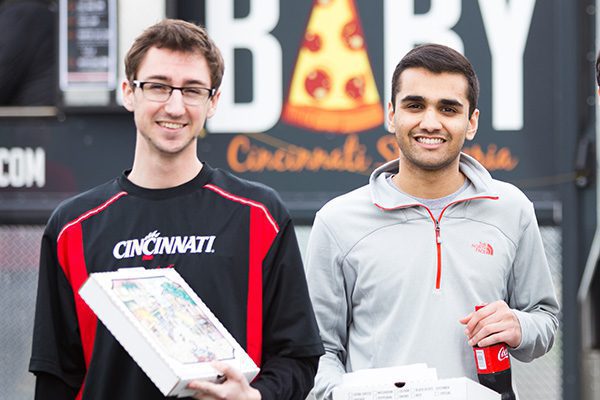 Two smiling male associates enjoying a pizza food truck in the parking lot at Standard Textile.