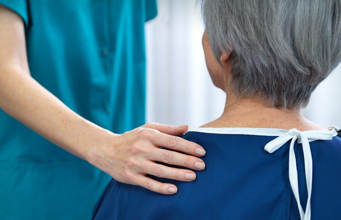 Nurse comforting patient with hand on older woman's shoulder