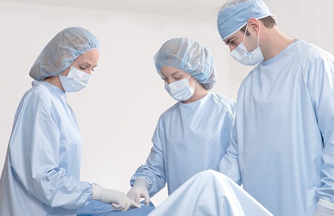 Three surgical clinicians wearing reusable surgical gowns and face masks