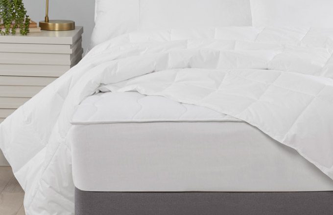 Hotel duvet insert draped on top of a bed with luxury mattress pad