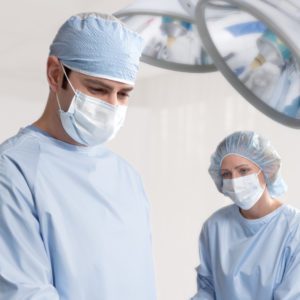 Nurse and Surgeon in operating room setting wearing blue reusable surgical gowns and masks.