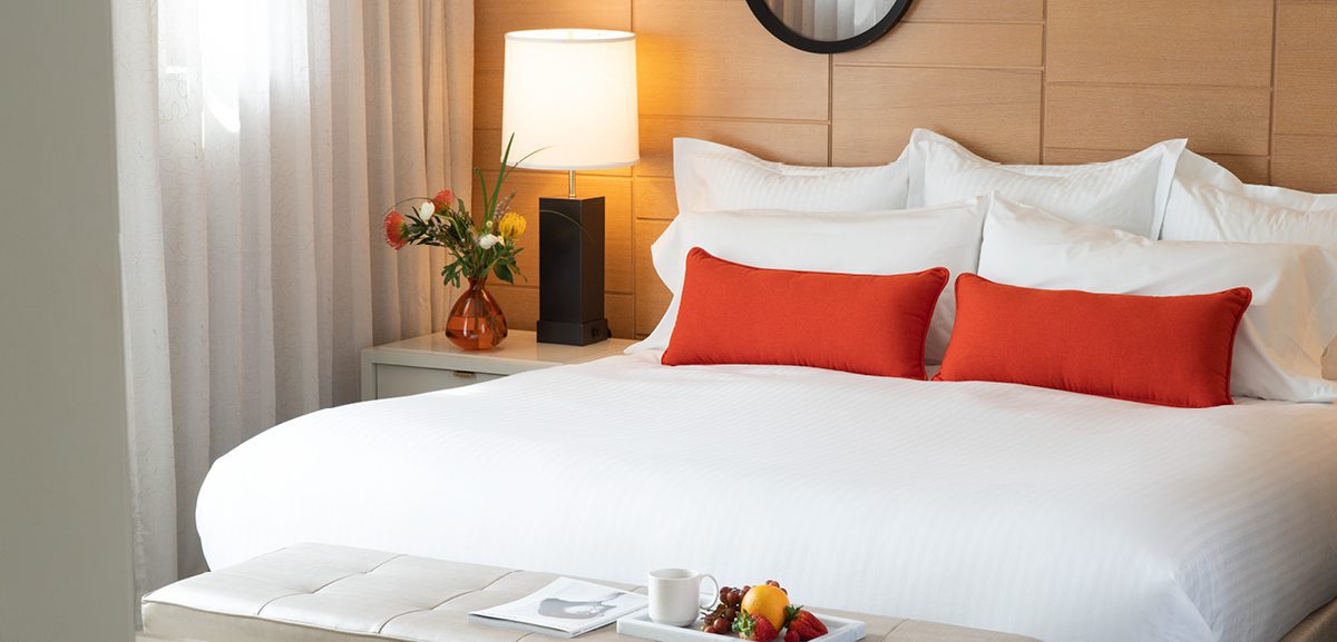 well made hotel bed with orange accent throw pillows