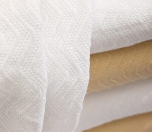 A stack of herringbone blankets in white and champagne are lightweight blankets.