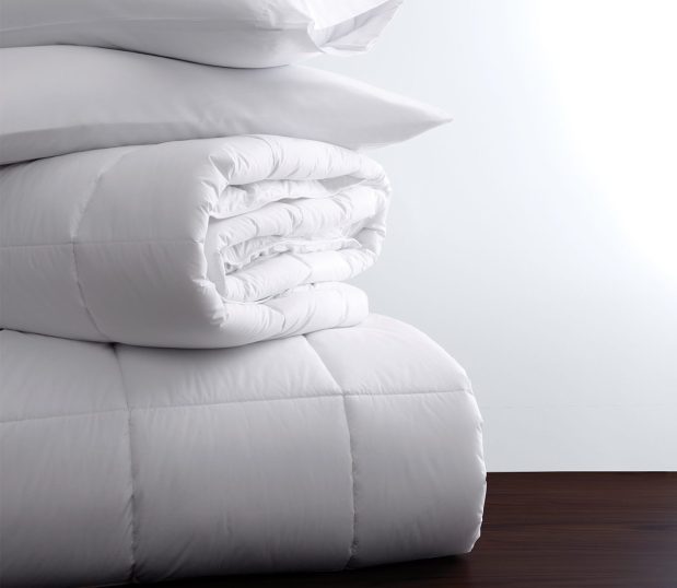 A stack of white bedding featuring Luxsoft a luxury comforter. This comforter is filled with a 100% Recycled Down Alternative.