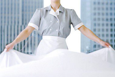 Hotel housekeeper spreads a sheet across a guest bed.