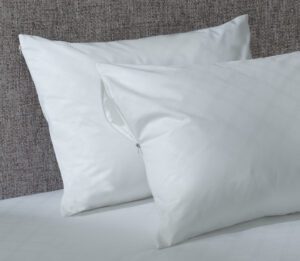 Two pillows featuring antimicrobial pillow covers are stacked against a headboard on a bed.