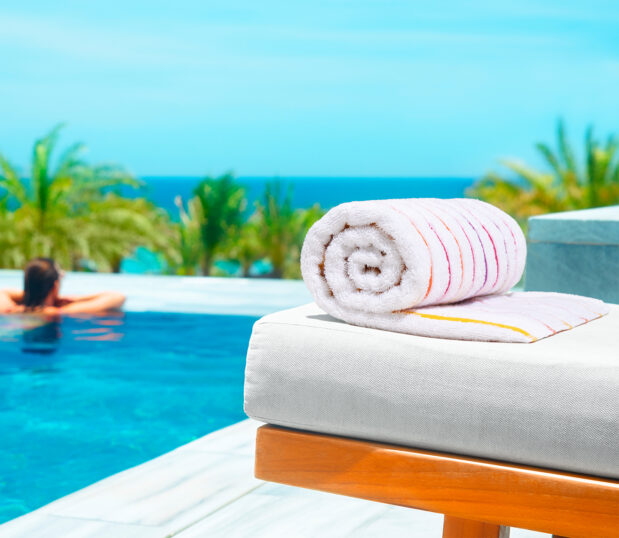 Sunrise stripe pool towel rolled on a lounge chair with a hotel pool in the background.