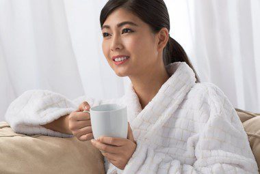 A woman with a cup of coffee relaxing in a soft cotton bath robe.