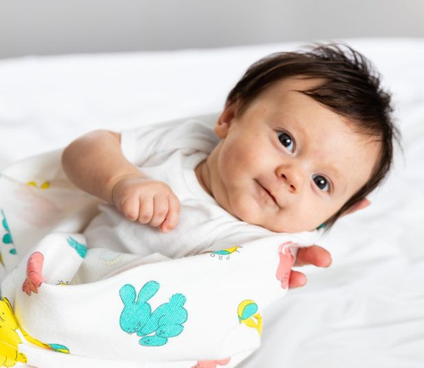 Cute dark haired baby being swaddled in our Bunnyland baby blanket..