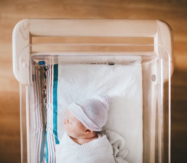 Our Striped Baby Blankets feature a cotton-rich fabric made to provide all the softness and warmth required for life’s first moments. Featuring classic pink & blue stripes. Shown here: an infant in a bassinet laying on the baby blanket.