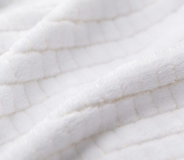 This is a detail shot of the Geometric dual tone robe. This white polyester robe has an offset, raised square pattern. Between the tufts the color of the robe is beige.