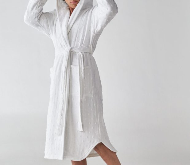 This image shows a male model wearing one of the white Heidi Weisel robes. The hood, scalloped hem and polka-dot pattern differentiate this robe.