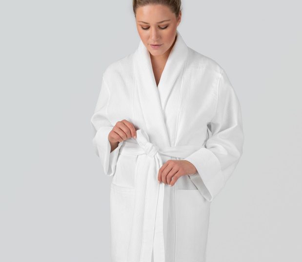 Model shown here wearing the Logan Bathrobe by Heidi Weisel robes. This unisex waffle robe is white, cotton and features pockets and cuffed sleeves.