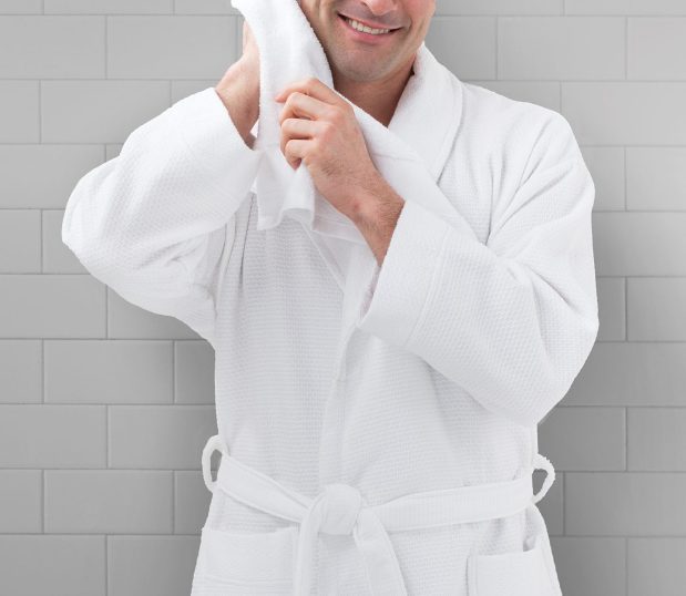 A photo of a man wearing a white, honeycomb bathrobe. He is rubbing his head with a towel suggesting he just got out of a shower.