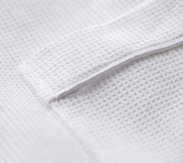 Detail of the pocket of the spa Waffle bathrobe. The familiar waffle weave design is complemented with white satin piping.