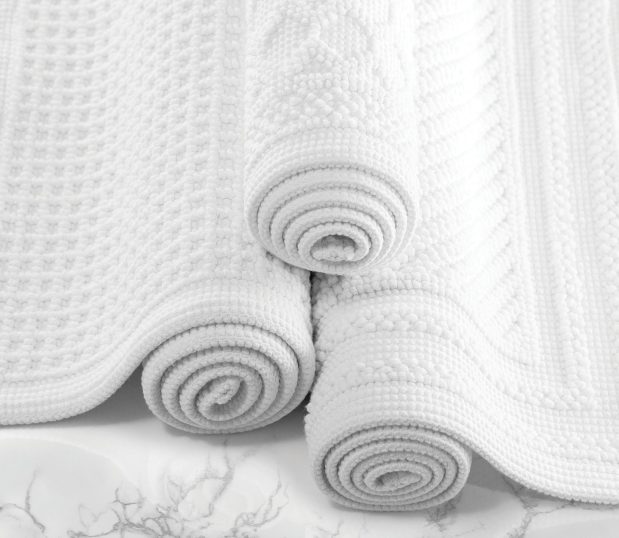 Three luxury bath rugs with different patterns artfully rolled to emphasis their textures.