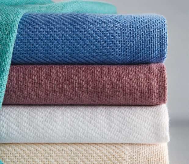 WIth a woven block pattern, the Snagless Hospital Blanket is shown here in a stack of 5 colors Blue, Cream, Rose, Teal, & White.