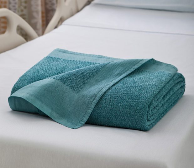 The Dual Cover® Blanket is shown here folded laying on a hospital bed.