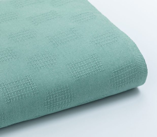 The Elite hospital blanket is shown here folded. It is emerald in color and has a woven pattern of rectangles and ovals.