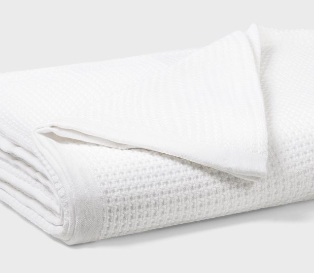 An image of a folded white cotton waffle blanket. This all-purpose waffle blanket is perfect for all seasons and climates.