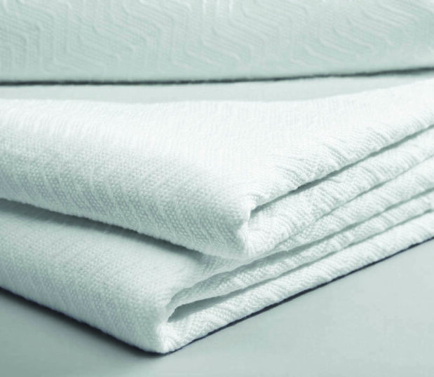A stack of white PerVal Herringbone hospital blankets. This densely woven herringbone pattern provides excellent thermal retention