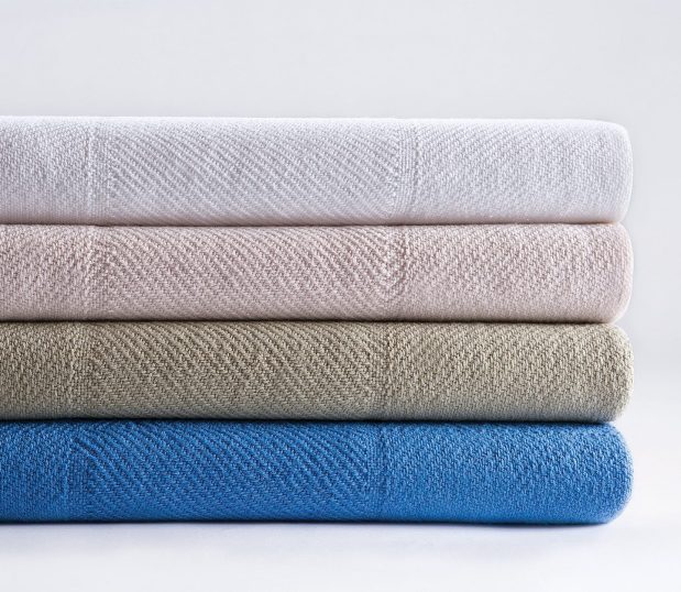 A stack of Serenity™ Spread blankets is shown with four of the available colorways. This hospital blanket features large woven squares.