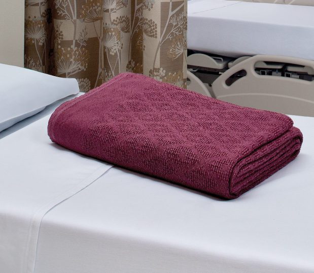 The Thermo Plus® Spread Blanket with it's distinguished woven diamond pattern shown here folded n a hospital bed. These hospital blankets are available in Beige, Emerald, Federal Blue, Natural, White, and Winter Wine.