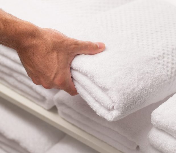 Image shows a hand taking a towel off of a linen shelf. ControlTex TMS Linen Inventory Management Software helps you effectively manage your linen system and brings cost savings.