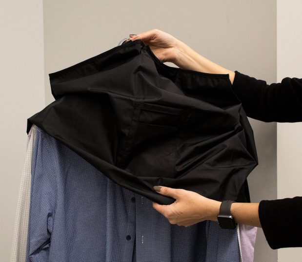 This image shows the VersaValet Hybrid Garment & Laundry Bag being put over hanging shirts.