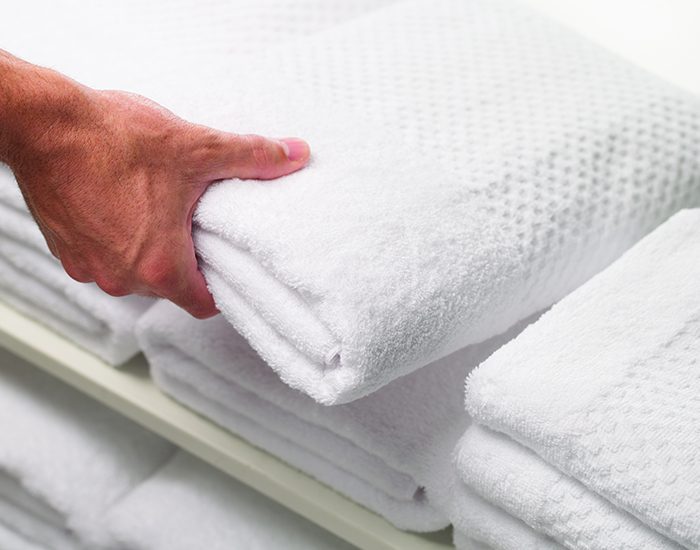 A hand is seen taking a white towel from a stack of white hotel towels.