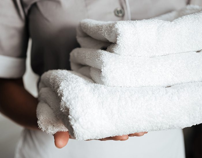 A hotel housekeeper is carrying a stack of white hotel towels.