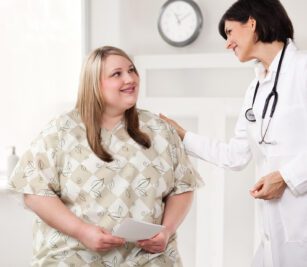 Image of patient waring a Bariatric E*Star® Patient Gown talking to her female doctor. These bariatric hospital gowns are a double lapover V-neck design.