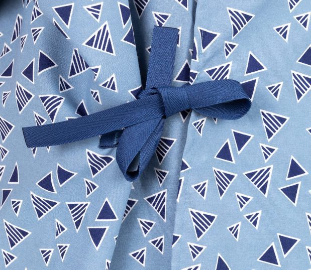 This is a detail of the Keystone E*Star® Patient Gown pattern. Thee Keystone pattern has a chambray field with triangles in dark blue with white outlines.The ties are dark blue.