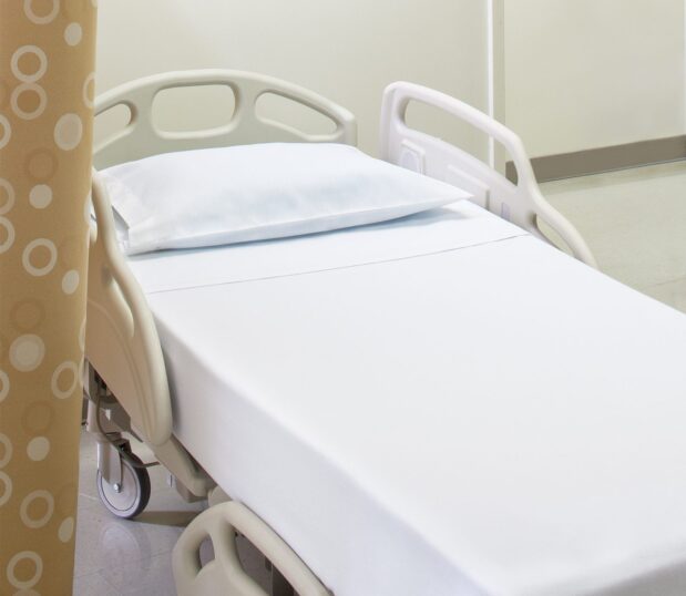 Excel® Hospital Sheeting for hospitals and health systems. Shown here on a hospital bed. Available in flat sheet, pillowcase, contour sheet, or draw sheet.