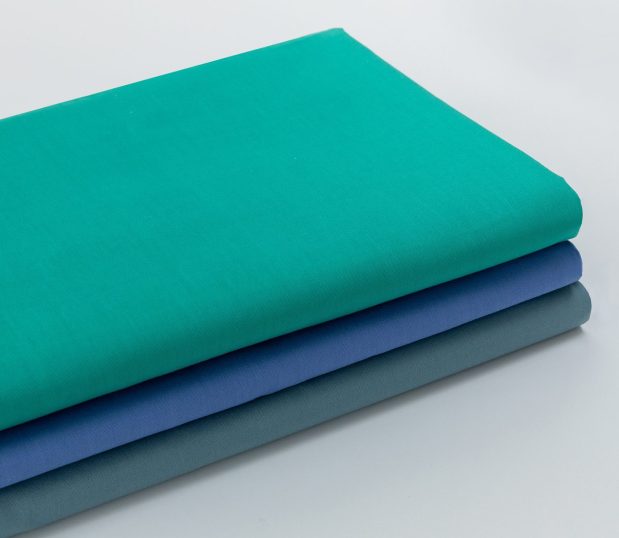 Excel® Vat Dyed Colored Hospital Sheeting. Folded stack of flat sheets shown in the three available colors: Jade Green, Ceil Blue, and Misty Green.