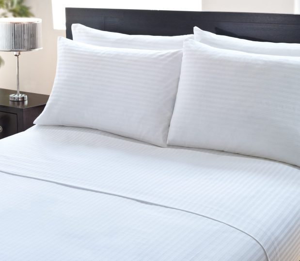 Luxury striped sheets and pillows on a hotel bed with dark wood headboard. These T300 sheets are 100% combed, long-staple and ring-spun cotton.