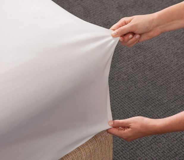 The Versatility fitted sheet is on a bed and being pulled to show how stretchy the sheet is. This fitted sheet alternative has no elastic to wear out.