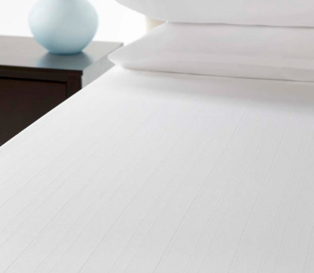 The Microstripe top cover is an ideal choice for hotels looking to brighten their guest rooms without breaking their budget. Image shows a microstripe top cover on a bed.