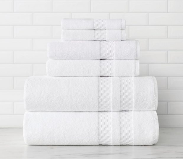 This is a stack of white luxury bath towels, hand towels and wash towels. The dobby bands near the hems feature a raised square pattern.